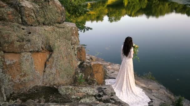 Jeune mariée debout sur la rive rocheuse, coucher de soleil — Video