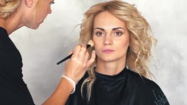 Genç bir kadının yüzünde bir allık makyaj sanatçısı koyar