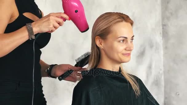 Парикмахер сушит волосы молодой блондинки — стоковое видео