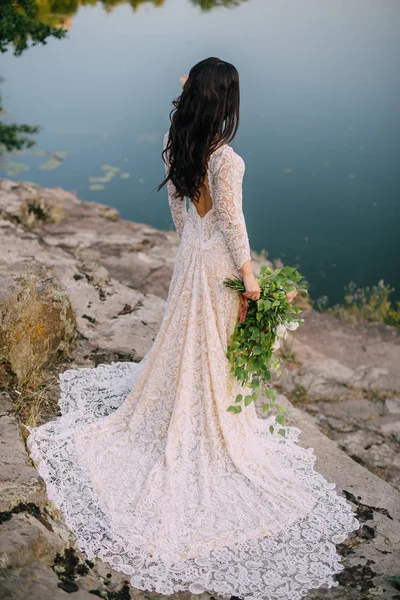 Jeune mariée debout sur la rive rocheuse, coucher de soleil — Photo