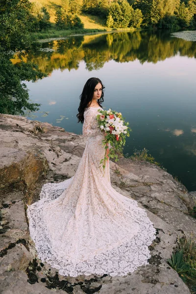 Jeune mariée debout sur la rive rocheuse, coucher de soleil — Photo