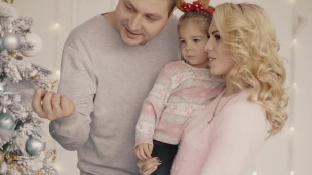Familia joven y feliz de mamá, papá y niña decorar un árbol de Navidad — Vídeo de stock