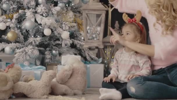 Jonge moeder met haar dochter zit in de buurt van de kerstboom — Stockvideo