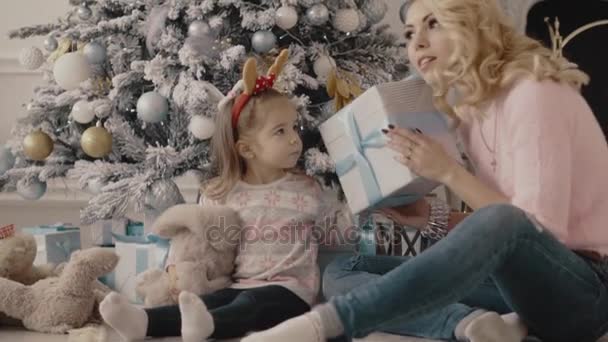 Маленька дівчинка дивиться на різдвяні подарунки зі своєю мамою — стокове відео