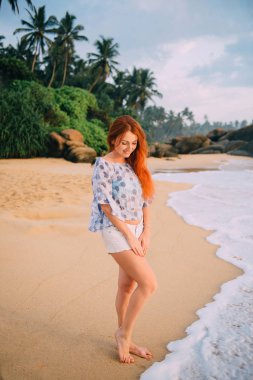 okyanus tarafından ayakta ve gülümseyen genç Kızıl saçlı kadın