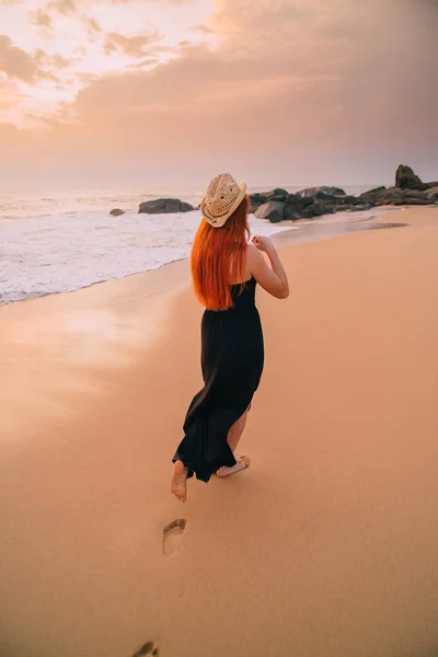 Junge Frau geht bei Sonnenuntergang am Strand entlang, Rückansicht — Stockfoto