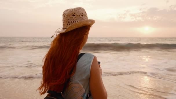 Молода жінка турист фотографує захід сонця біля океану — стокове відео
