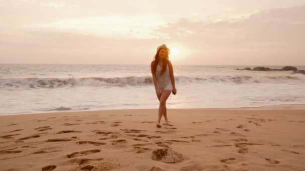 Νεαρή γυναίκα τουριστικές περπατώντας κατά μήκος της παραλίας του ωκεανού στο ηλιοβασίλεμα — Αρχείο Βίντεο