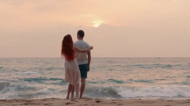 Jeune couple admirant le coucher de soleil sur le bord de l'océan, face arrière — Video