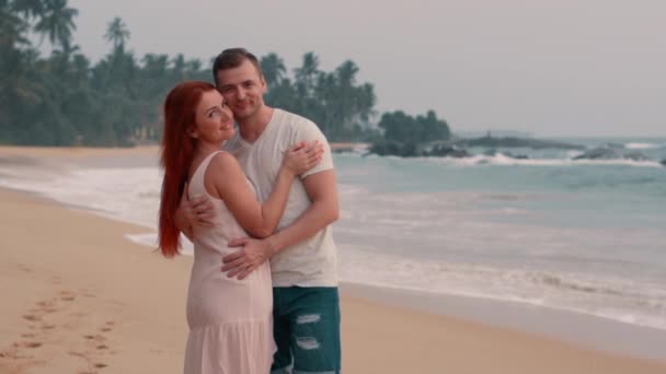 Молодая счастливая пара, обнимающая на берегу океана на закате — стоковое видео