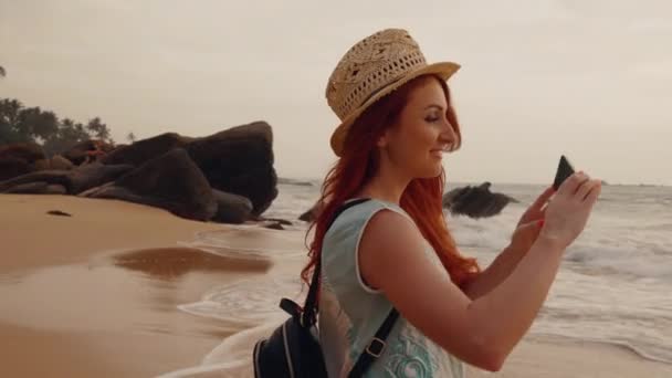 Young woman tourist taking pictures of the sunset by the ocean — Stock Video