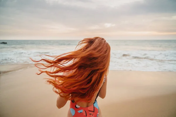 Молода руда жінка з літаючим волоссям на океані, вид ззаду — стокове фото