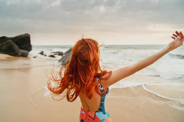 Nuori punatukkainen nainen, jolla lentävät hiukset meressä, peruutusnäkymä — kuvapankkivalokuva