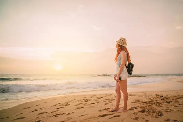 Молода жінка ходить уздовж пляжу на заході сонця, вид ззаду — стокове фото