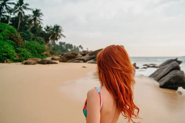 stock image young red-haired woman with flying hair on the ocean, rear view