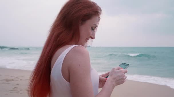 Νεαρή γυναίκα απολαμβάνει ένα smartphone σε μια τροπική παραλία — Αρχείο Βίντεο