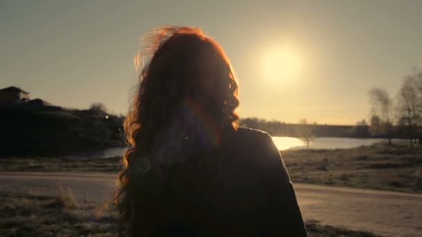 Молодая рыжеволосая женщина, стоящая на фоне природы, спиной к камере — стоковое видео