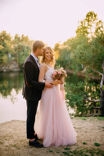 Feliz recém-casados de pé contra o fundo da natureza ao pôr do sol — Fotografia de Stock