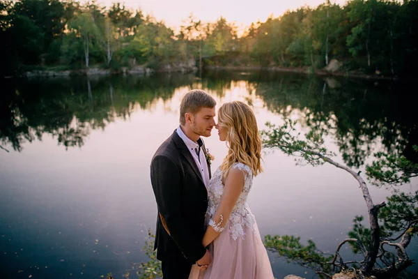 Gelukkig jonggehuwden staande op de oever van het meer bij zonsondergang — Stockfoto