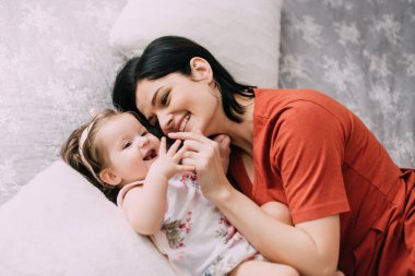 Genç anne, bir yaşındaki kızıyla yatakta eğleniyor, yakın plan.