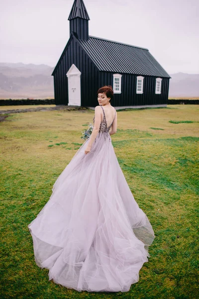 Gelinlik giymiş gelin kilisenin yanında duruyor. Sırtı kameraya dönük, İzlanda. — Stok fotoğraf
