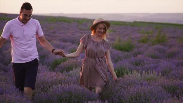 Dva milenci kráčejí po levandulovém poli a drží se za ruce. — Stock video