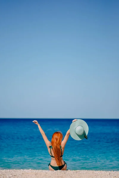 Onnellinen nainen innokkaasti nostaa kätensä istuu rannalla — kuvapankkivalokuva