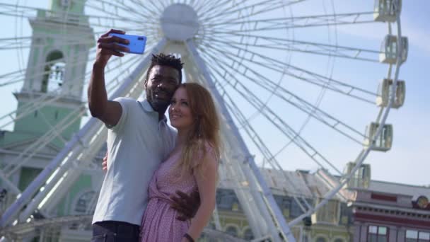 Νεαρό ζευγάρι κάνει selfie στο φόντο ενός τροχού λούνα παρκ — Αρχείο Βίντεο