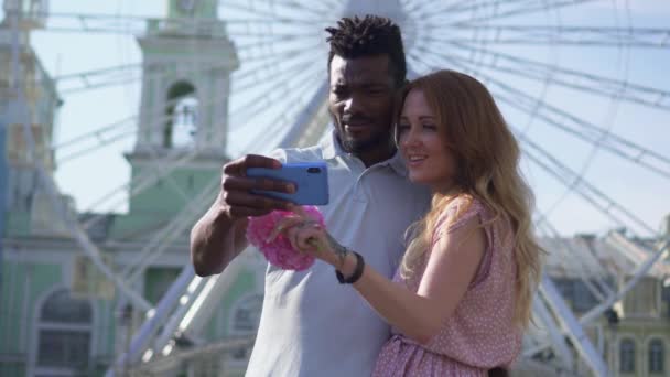 Ένα χαρούμενο ζευγάρι κοιτάζει την οθόνη του smartphone και γελάει στην πλατεία — Αρχείο Βίντεο