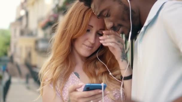 Gros plan d'un jeune couple écoutant de la musique sur un casque dans la rue — Video