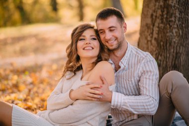 Sonbahar parkında çimlerin üzerinde oturan neşeli genç çift