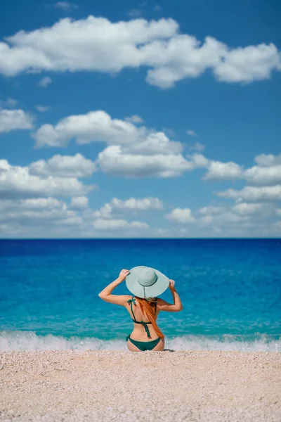 Молода жінка сидить на пляжі і дивиться на море, вид ззаду — стокове фото