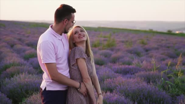 Joven abraza a su novia de pie en un campo de lavanda floreciente — Vídeos de Stock