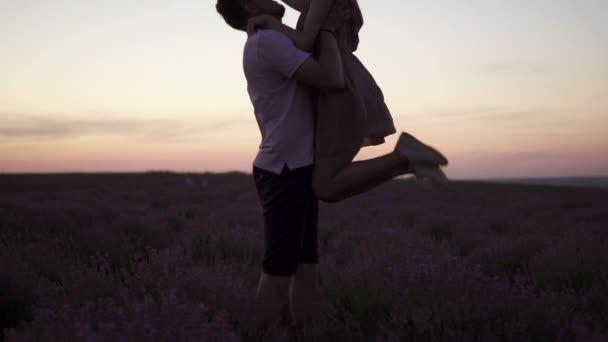 Silhouette A young man raises his girlfriend in his arms standing in a flowering lavender field at sunset — Stock Video