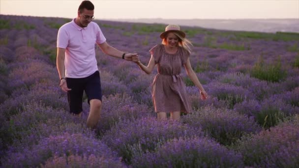 Dva milenci kráčejí po levandulovém poli a drží se za ruce. — Stock video