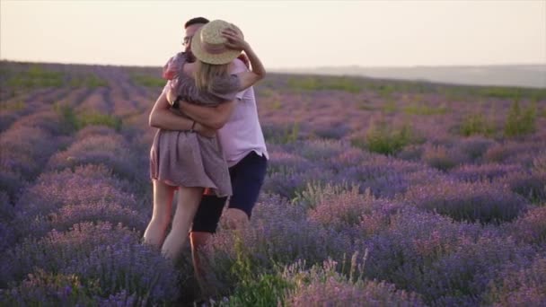 Un hombre joven está dando vueltas en sus brazos a su novia en un campo de lavanda floreciente, cámara lenta — Vídeos de Stock