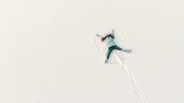 Top down luchtfoto van een jonge vrouw het maken van een sneeuw engel plezier — Stockvideo