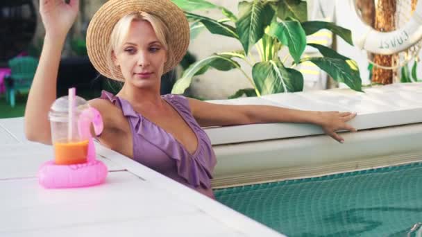Jeune belle femme se relaxe dans la piscine et boire du jus de fruits — Video