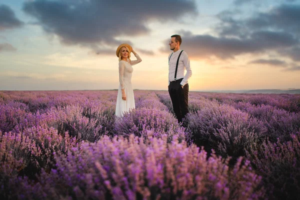 Šťastní novomanželé stojí v kvetoucím levandulovém poli při západu slunce — Stock fotografie
