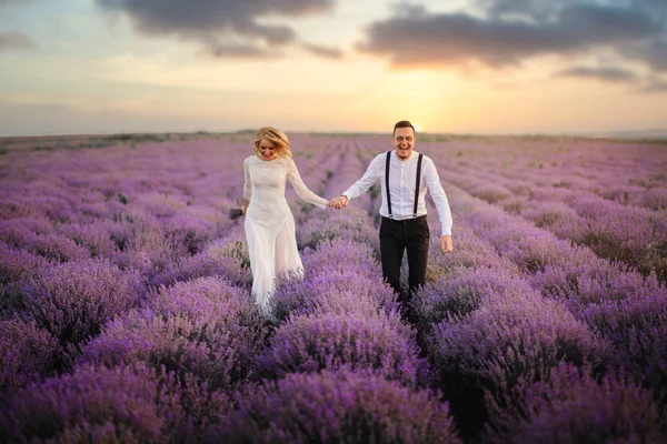 Joyeux jeunes mariés courant le long du champ de lavande en fleurs — Photo