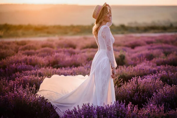 Ung kvinna i vit klänning går genom blommande lavendel fält vid solnedgången — Stockfoto