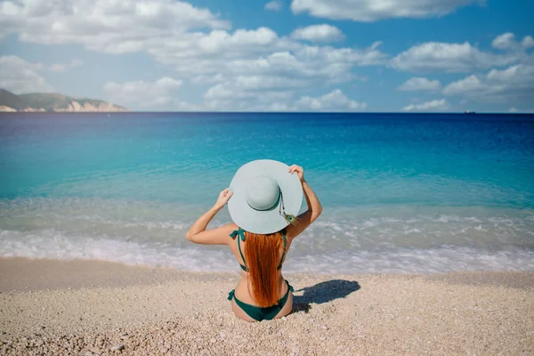 Nuori nainen istuu rannalla ja katsoo merelle, taakse — kuvapankkivalokuva