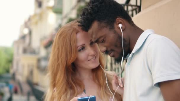 Крупный план молодой пары, слушающей музыку на наушниках на улице — стоковое видео
