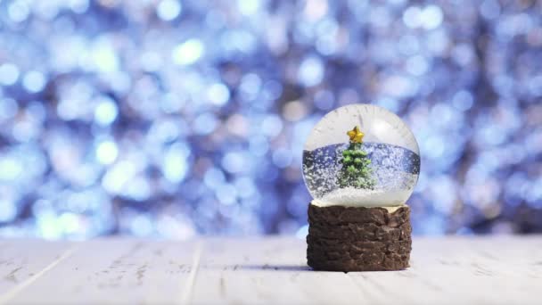 Close-up de flocos de neve girando em torno de uma árvore de Natal dentro de uma bola de vidro — Vídeo de Stock