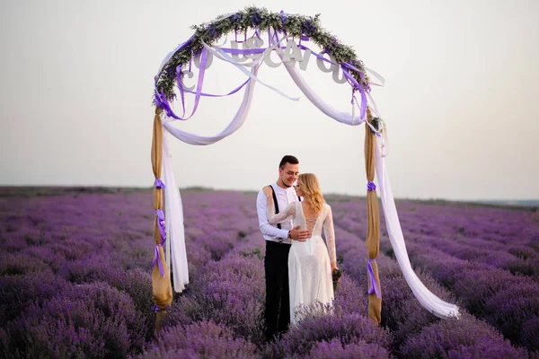 Jeune mariée heureuse et marié étreignant dans le champ de lavande en fleurs — Photo