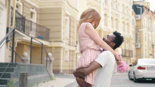 Joven hombre negro levanta a su novia en sus brazos mientras camina en una calle de la ciudad — Vídeo de stock