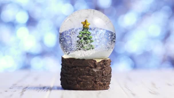 Primer plano de copos de nieve girando alrededor de un árbol de Navidad dentro de una bola de vidrio — Vídeos de Stock