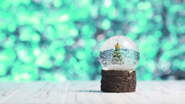 Primer plano de copos de nieve girando alrededor de un árbol de Navidad dentro de una bola de vidrio — Vídeos de Stock