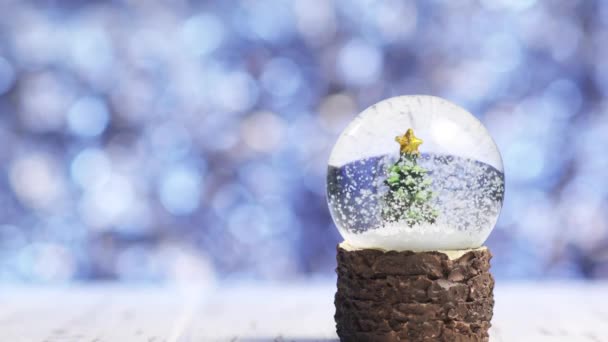 Close-up de flocos de neve girando em torno de uma árvore de Natal dentro de uma bola de vidro — Vídeo de Stock