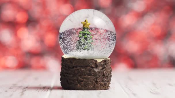 Hópelyhek keringenek egy karácsonyfa körül egy üveggömbben. — Stock videók